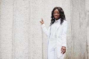 joven afroamericana, vestida de blanco, pared de piedra blanca de fondo foto