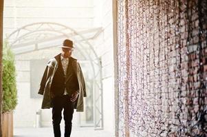 Fashion portrait of black african american man on green velvet jacket, black hat and coat cloak on his shoulders posed at arch tunnel photo