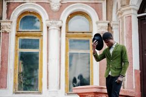 Fashion portrait of black african american man on green velvet jacket stay on stairs and wear his black hat background old mansion. photo