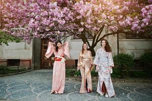 tres chicas europeas con kimono japonés tradicional flor de fondo rosa árbol de sakura foto