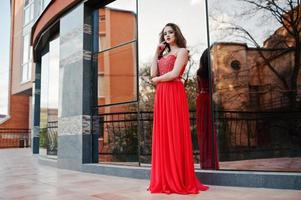 Portrait of fashionable girl at red evening dress posed background mirror window of modern building photo