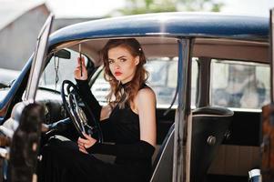 retrato de una hermosa modelo de moda sexy con maquillaje brillante en estilo retro sentado en un auto antiguo con un cigarrillo en la mano. foto