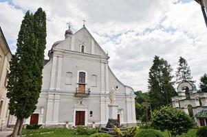 White stone catholic church with a bell tower and monument of Holy Mary photo