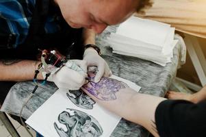 el maestro del tatuaje hace un tatuaje para un hombre rockero en el salón de tatuajes foto