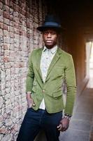 Fashion portrait of black african american man on green velvet jacket, black hat posed at arch tunnel on sunset. Vertical photo