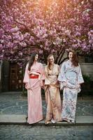 Three european girls wearing traditional japanese kimono background blossom pink sakura tree photo