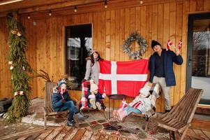 familia con banderas de dinamarca cerca de la casa de madera. viajar a países escandinavos. los daneses más felices. foto