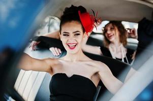 Three young girl in retro style dress seat on old classic vintage car and having fun emotions photo