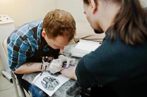 el maestro del tatuaje hace un tatuaje para un hombre rockero en el salón de tatuajes foto