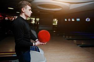 Young man holding a bowling ball standing against bowling alleys with ultraviolet light. photo