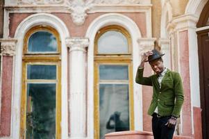 Fashion portrait of black african american man on green velvet jacket stay on stairs and wear his black hat background old mansion. photo