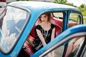 Portrait of beautiful curly fashion girl model with bright makeup in retro style sitting on a vintage car photo