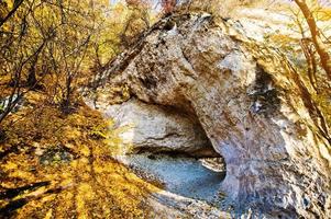 cueva de montaña de piedra caliza en el bosque de hojas amarillas foto