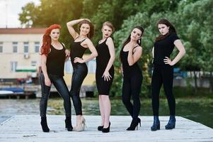 cinco hermosas jóvenes modelos de chicas sexy en vestido ajustado negro posando en el muelle foto