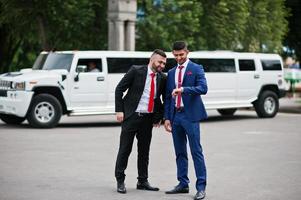 Two stylish arabic businessman mans in tuxedo background white Hummer limousine photo