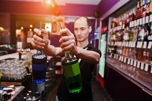 joven barman sosteniendo botellas de cóctel en el bar foto