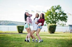 Three happy girls in short shorts and wreaths on heads dancing and having fun on green grass at bachelorette party photo