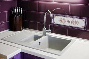 Kitchen mixer tap into granite work surface background violet tile and knifes photo