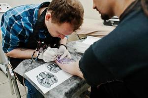 el maestro del tatuaje hace un tatuaje para un hombre rockero en el salón de tatuajes foto