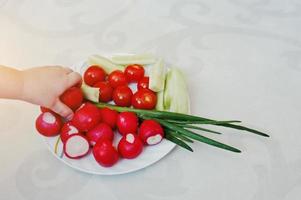 mano de niño en el plato con verduras de primavera sobre fondo de decoración blanca foto
