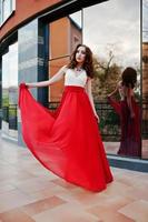 Portrait of fashionable girl at red evening dress posed background mirror window of modern building photo