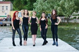 Five beautiful young sexy girls models in black tight dress posing on pier photo