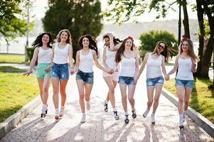 Seven happy and sexy girls on short shorts and white shirts running fun on road at park on bachelorette party photo