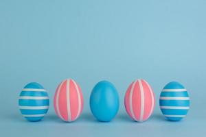 Five Easter blue and pink eggs with white stripes on blue background. photo