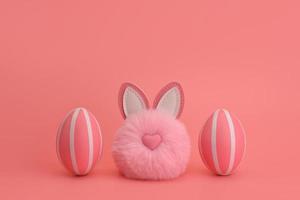 An Easter pink fluffy rabbit pom-pom between two pink striped eggs. photo