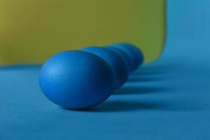 Five blue painted Easter eggs lie diagonally on a blue and yellow background. Deep shadows. photo