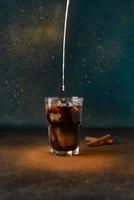 Milk is pouring into a glass cup with cold coffee. photo