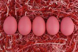 Five pink Easter eggs in a row on striped paper in red and pink tones photo