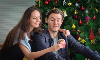 In the concept picture, Christmas gifts. White Caucasian woman presents a gift in a red box to a young man or lover. happy when received a gift photo