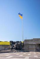 National flag of ukraine with monument statue against clear blue sky photo