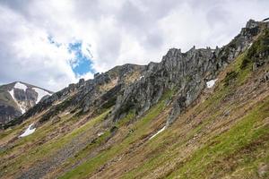 Rock cliff covered with moss over steep slope and hill against cloudy sky photo