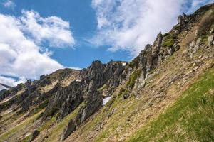 Rock cliff covered with moss over steep slope against cloudy sky photo