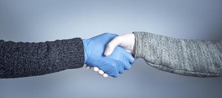 el concepto de un apretón de manos seguro. estrechar la mano con guantes médicos sobre fondo gris. foto