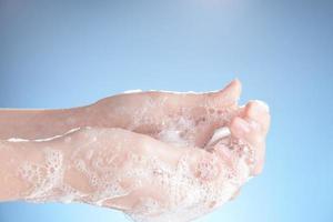 Woman hands in soapsuds, on blue background close-up. photo