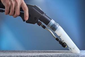 The hand holds the hoover. Washing carpet with hoover close-up on blue background. photo