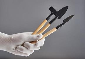 Hand in new pure white glove holding gardening tools isolated on gray background. photo