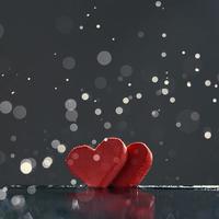 Two red hearts with rain drops reflected in the water on a dark background with a bokeh. Photo with copy space.