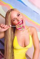 blonde woman with african braids and with lollipop in her hands in yellow dress