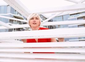 portrait of pretty cool beautiful short hair blonde woman in red coral dress near wooden white arbor for the beach photo