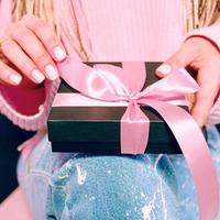 manos de mujer con manicura rosa sosteniendo una caja de regalo negra con cinta rosa foto