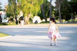 Rear back view of kid girl is jogging in evening at public park. Child wear cloth face mask that can insert filters for PM2.5 dust and prevent viruses. photo