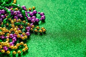 Mardi Gras concept. Multi-colored beads on green shiny background. photo