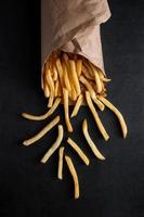 Hot crispy fries in a paper bag on black background. photo