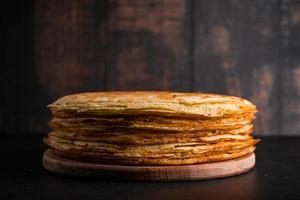 A stack of thin pancakes on a dark wooden background. photo