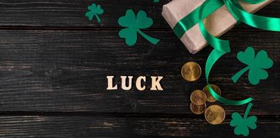 The word luck, clover shamrock and gift with a green ribbon on a dark wooden background. photo