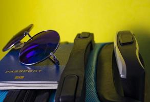 Sunglasses and Passport Close-up on a Blue Suitcase on a Yellow Background. Summer Travel Concept.